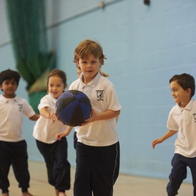 child holding a basketball with 3 other children running across the hall